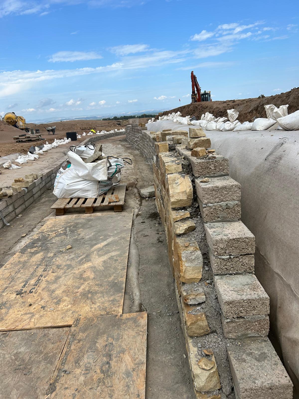 Natural stone facing on block retaining wall with excavator in background