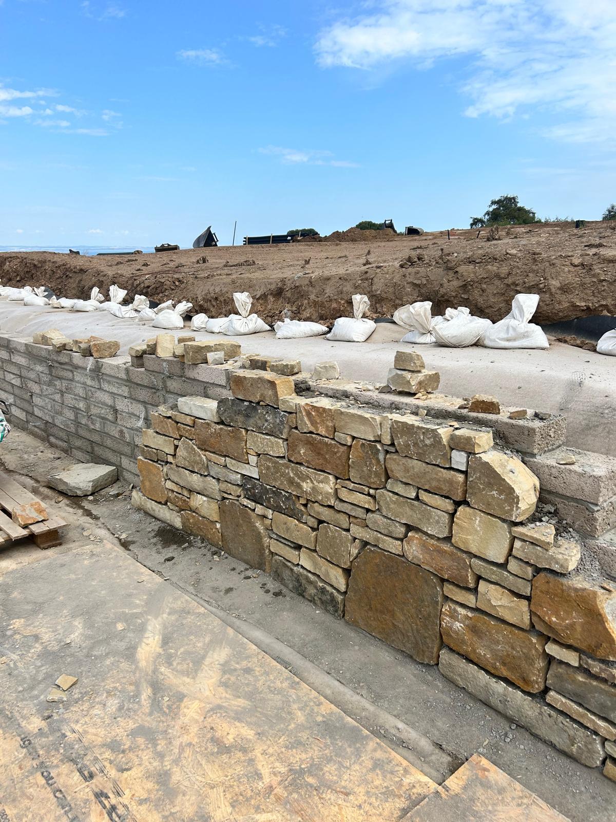 Natural stone facing being applied to retaining wall on development site